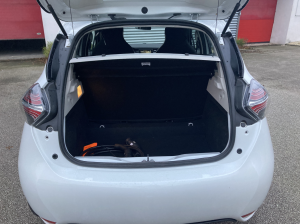 Coffre ouvert d’une Renault Zoé blanche avec câble de recharge visible à l’intérieur